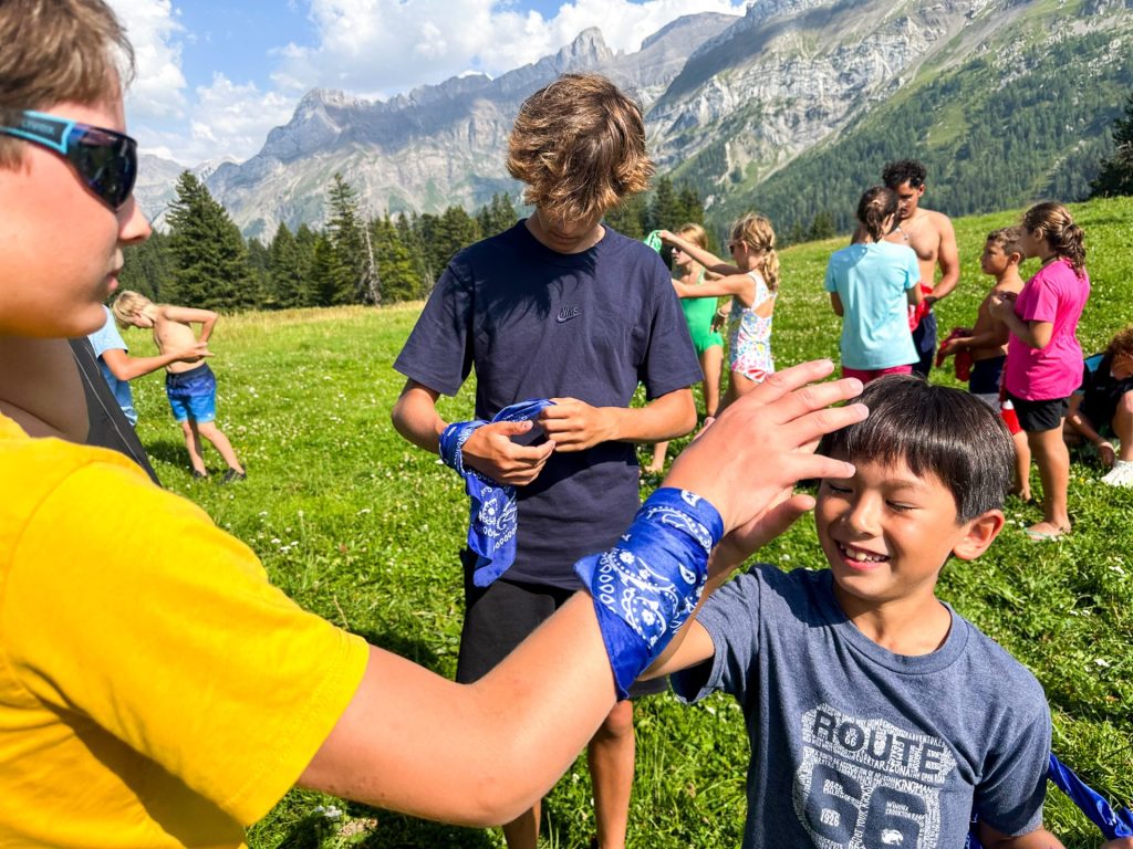 Campistas atándose pañuelos de equipo antes de un juego en un prado alpino