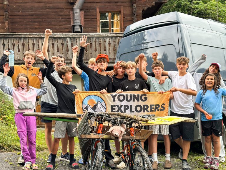 Camper jubeln mit dem Young Explorers Club Banner vor dem Chalet