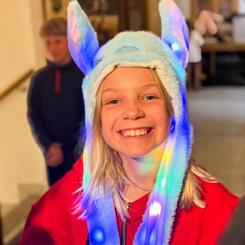 Smiling girl wearing a light-up bunny hat during an evening activity at camp