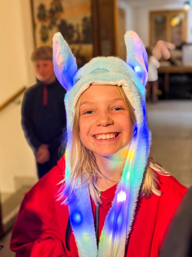 Smiling girl wearing a light-up bunny hat during an evening activity at camp
