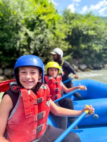 Two campers in helmets and life jackets rafting down an alpine river