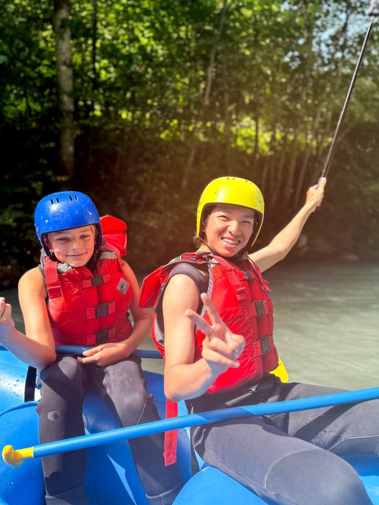 Campers raising their paddles while rafting on a river at summer camp