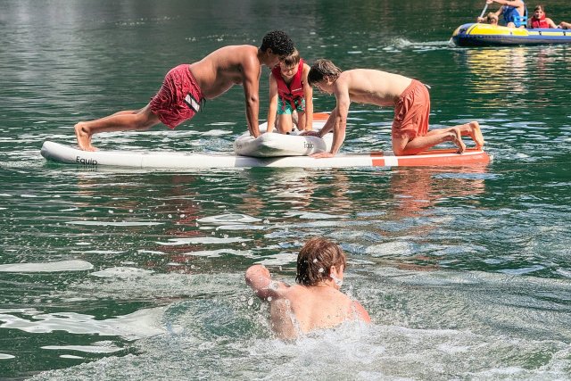 Ados en équilibre sur un paddle sur un lac de montagne pendant qu'un copain nage à côté