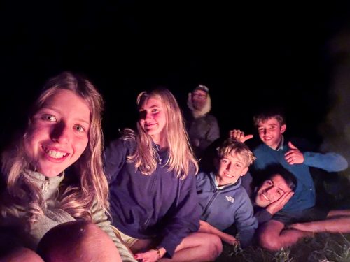 Teenagers gathered around the campfire at night on the Tour du Mont Blanc camp