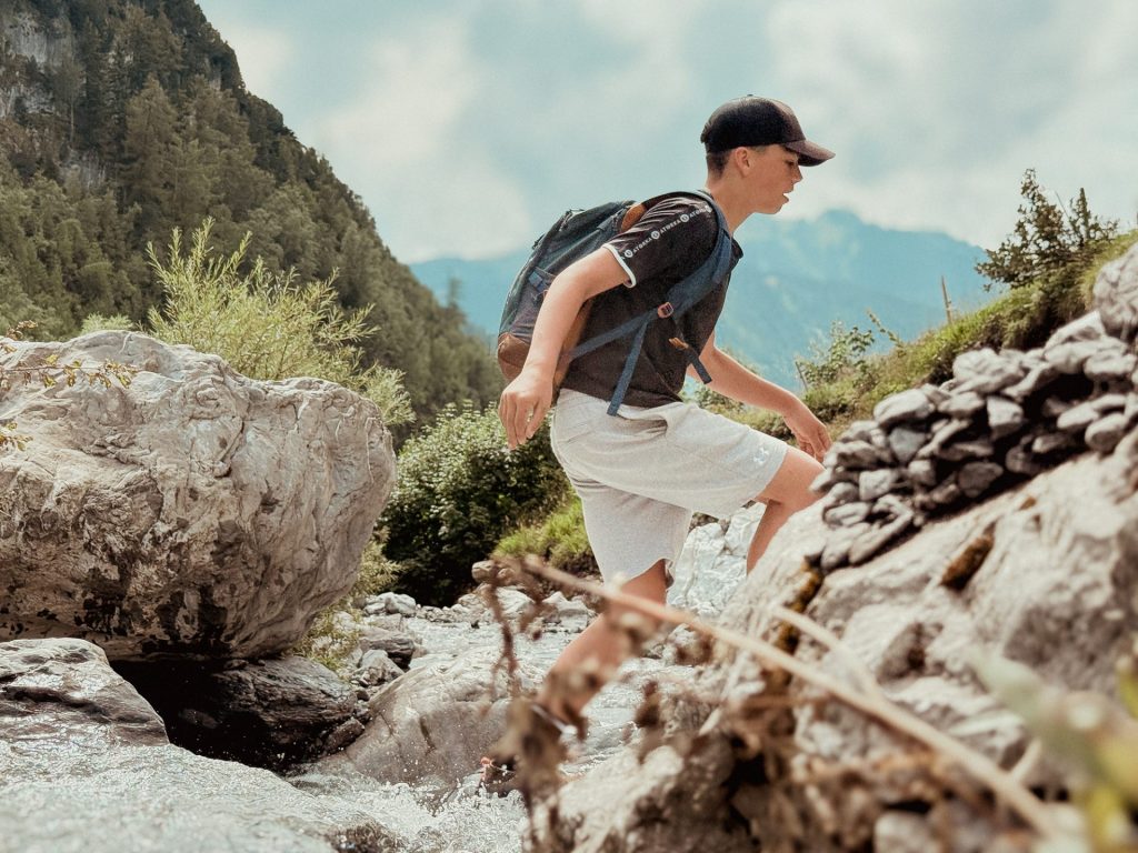 Teenager hiking across rocks beside a mountain stream