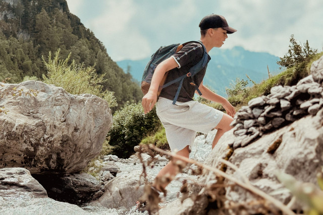 Teenager hiking across rocks beside a mountain stream