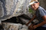 Boy with a headlamp exploring a cave entrance at the Survival Academy summer camp