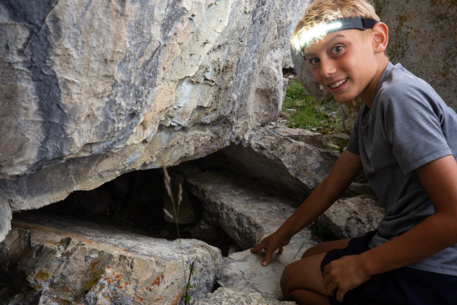 Boy with a headlamp exploring a cave entrance at the Survival Academy summer camp
