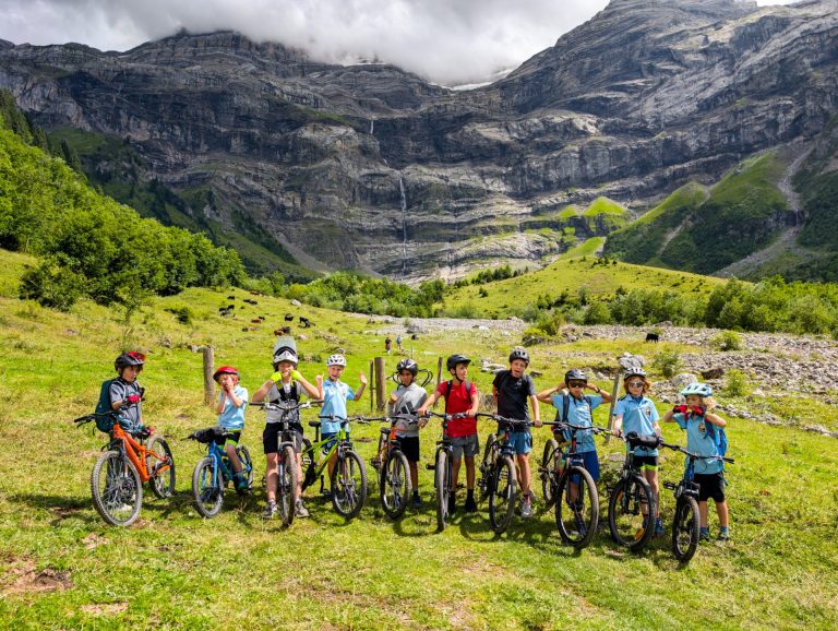 Jeunes campeurs alignés avec leurs VTT sous les falaises et cascades du Creux de Champ aux Diablerets