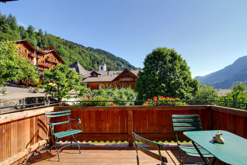 Terrasse en bois avec chaises bistrot dominant le village de Champéry et son clocher