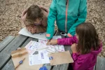 Children studying the maps and clues of a treasure hunt trail at a picnic table