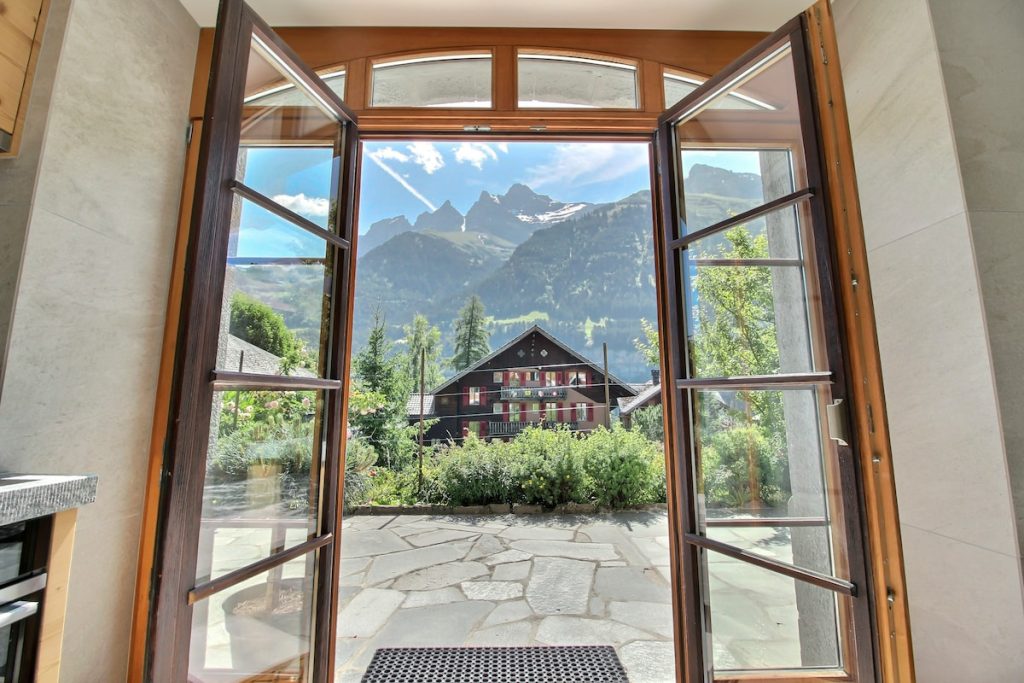 Portes-fenêtres de la cuisine ouvrant sur la terrasse en pierre, les Dents du Midi en arrière-plan