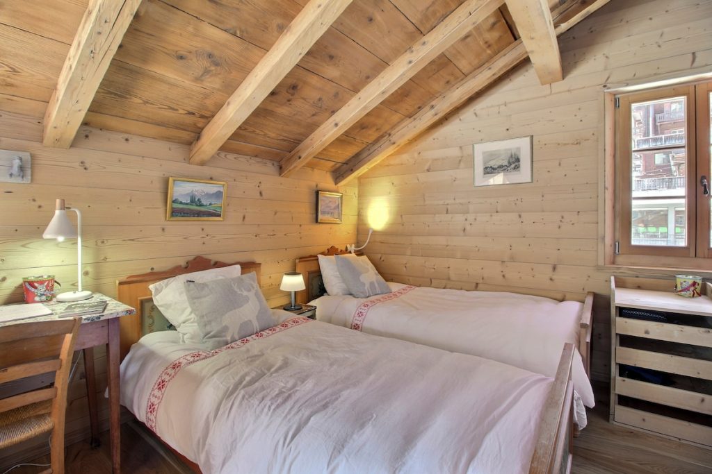 Chambre mansardée à deux lits avec poutres apparentes et linge brodé au chalet de Champéry