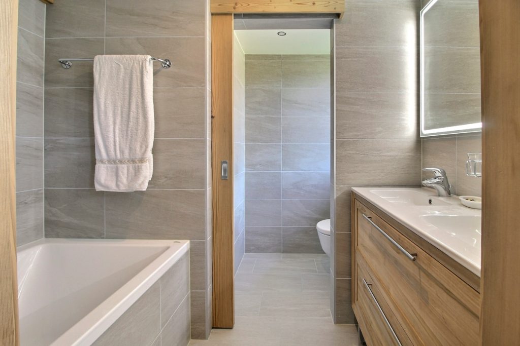 Salle de bains familiale avec baignoire, porte coulissante et meuble en bois au chalet de Champéry