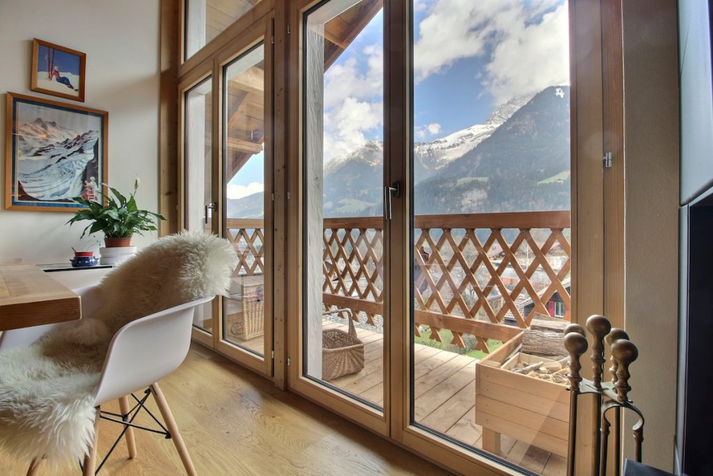 Fauteuil de lecture près d'une fenêtre ouverte sur le balcon et les montagnes de Champéry