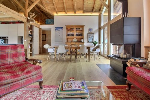 Living room with a red tartan sofa, dining table and wood stove in the family camp chalet