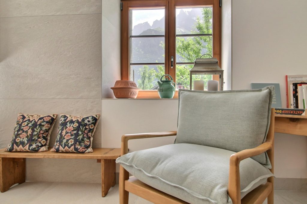 Coin tranquille avec banc en bois et fauteuil gris sous une fenêtre au chalet de Champéry