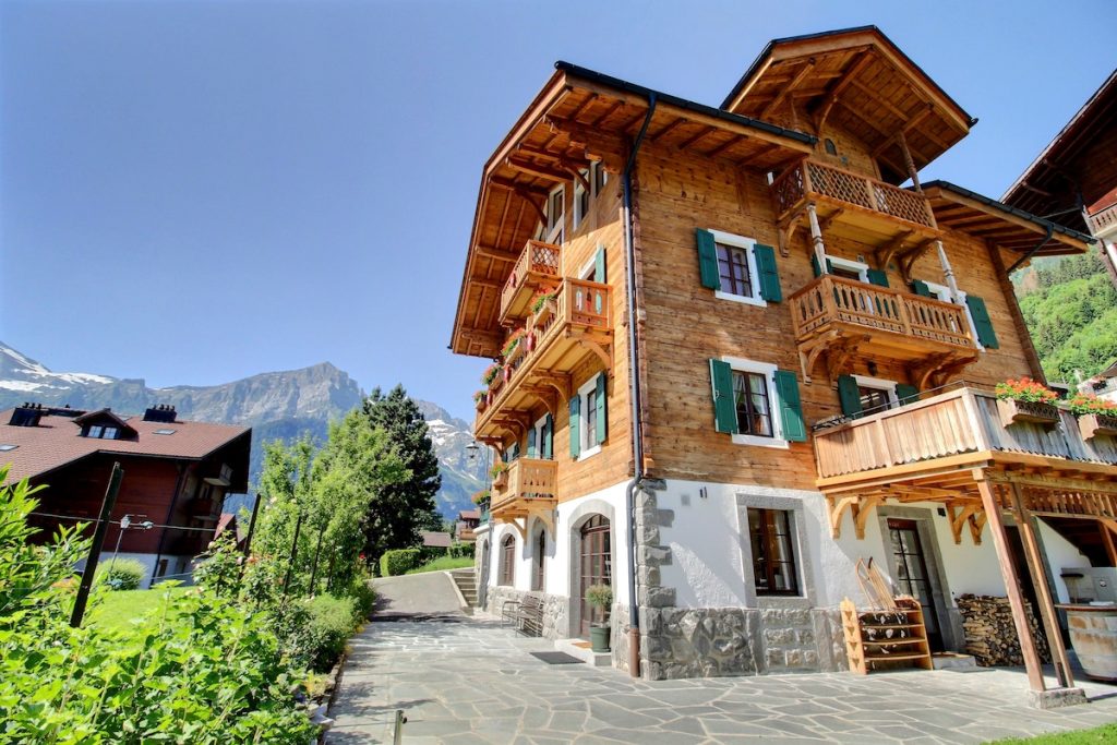 Grand chalet traditionnel aux balcons en bois et volets verts par une journée ensoleillée à Champéry