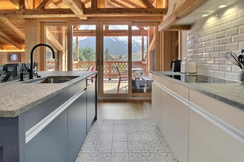 Kitchen with a blue island and granite worktop opening onto the terrace with a mountain view