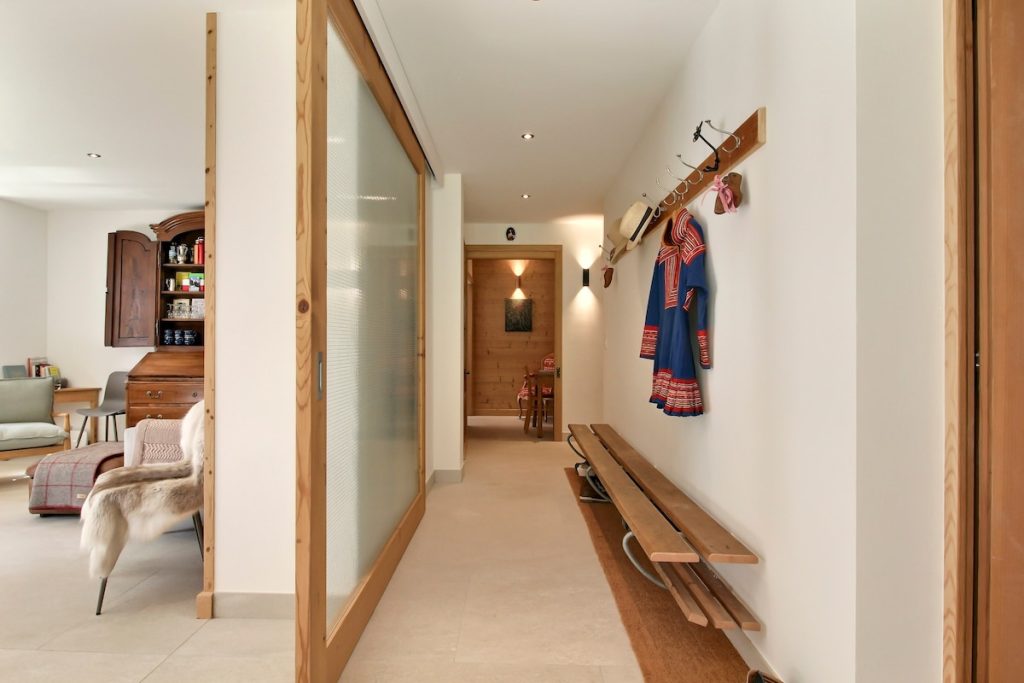 Hall d'entrée avec porte vitrée coulissante, banc en bois et patères au chalet de Champéry