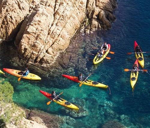Group of sea kayaks paddling through a rocky cove with crystal-clear water